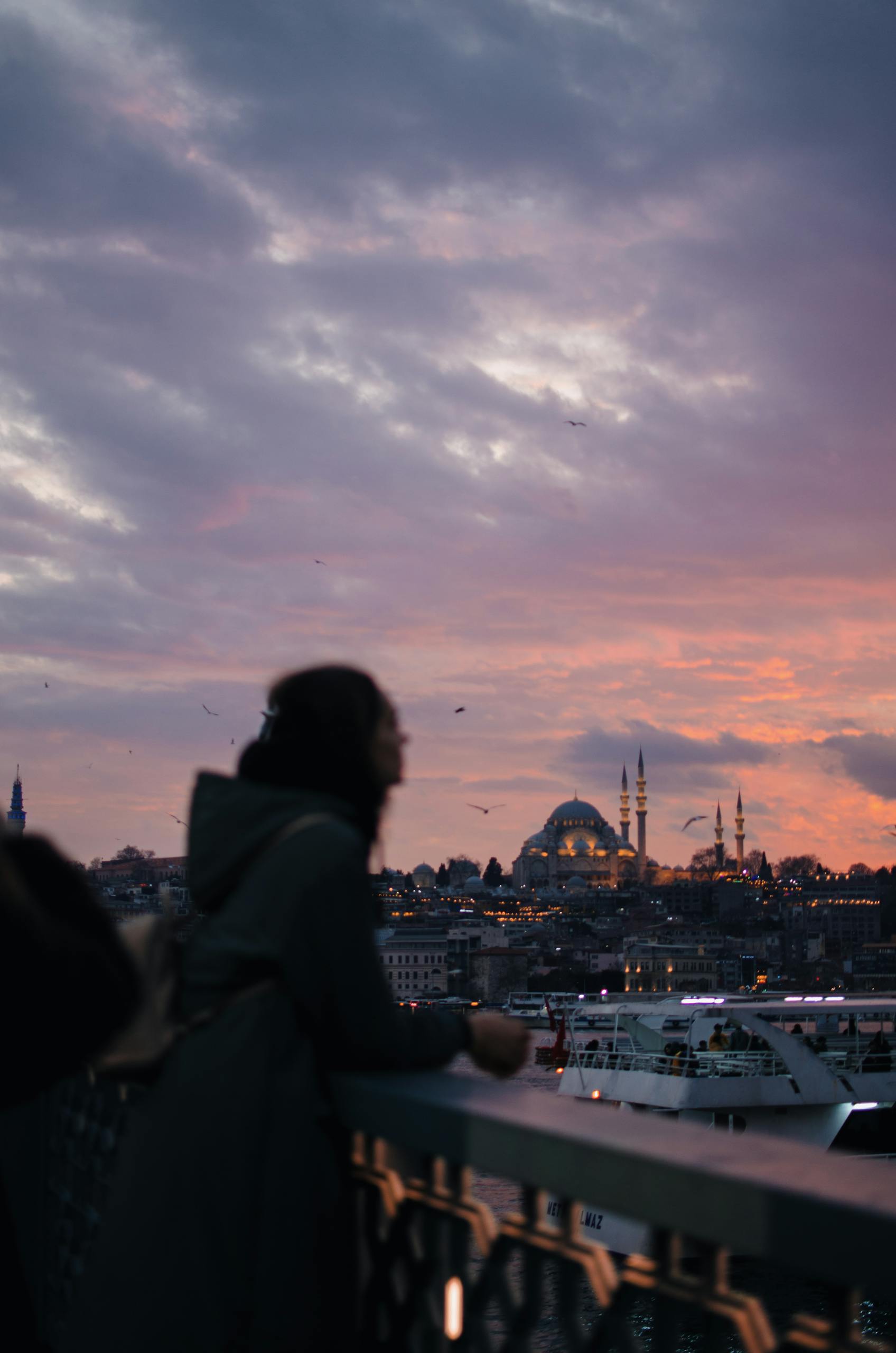 Anonymous woman observing city from bridge over river at sundown